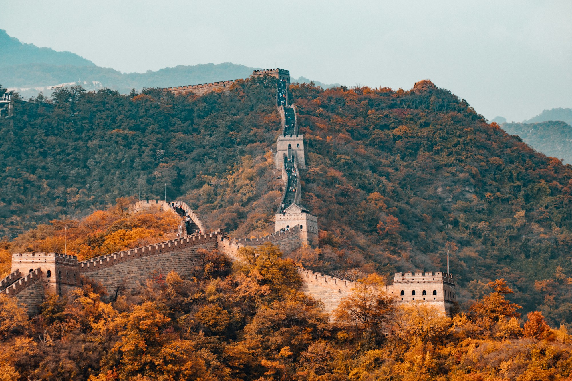 The Great Wall of China running along a forested ridge line into the distance.
